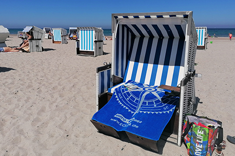 Strandkorb mit ECL-Badetuch in blau am Sandstrand. Im Hintergrund die Ostsee.
