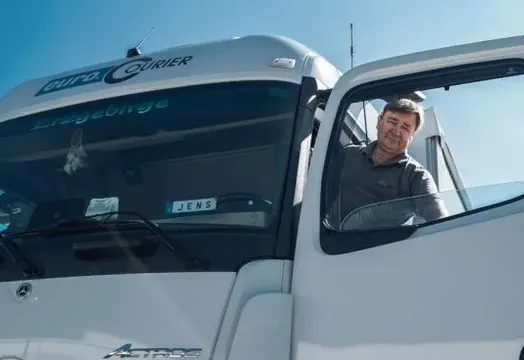 Ein LKW-Fahrer schaut aus dem Fahrerhaus und freut sich auf seine Touren.