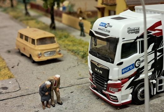 Der ECL Modelltruck von Herpa auf einer Modellplatte, lässt ein altes Ehepaar über die Straße gehen.
