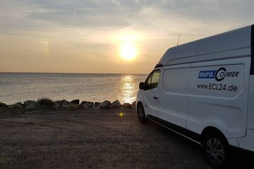 Am Meer steht ein Kurierfahrzeug bei Sonnenuntergang