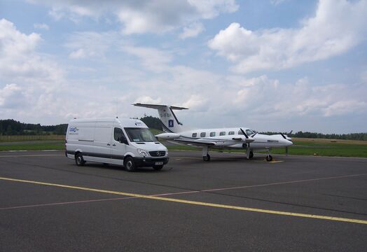 Luftfracht Anlieferung per Kleintransporter am Rollfeld neben einem Kleinflugzeug für Aircharter.