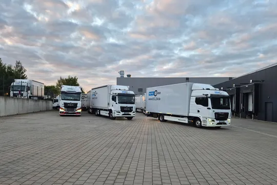 Drei abfahrbereite LKW auf dem Hof bei Sonnenaufgang.