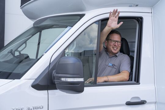 Ein freundlich lächelnder Transporter Fahrer grüßt aus seinem geöffneten Fenster.